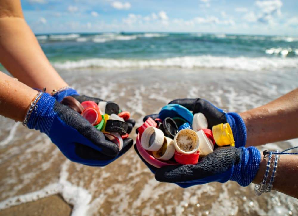 manos recogiendo plásticos en la playa